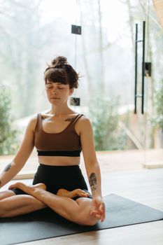 A woman in meditative yoga pose indoors on a mat, embracing serene mindfulness.