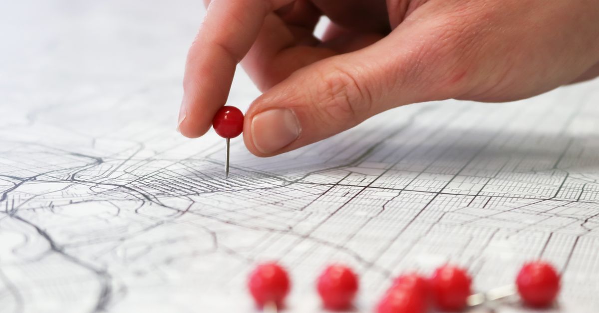 Hand placing a red pin on a map to mark a local service area location