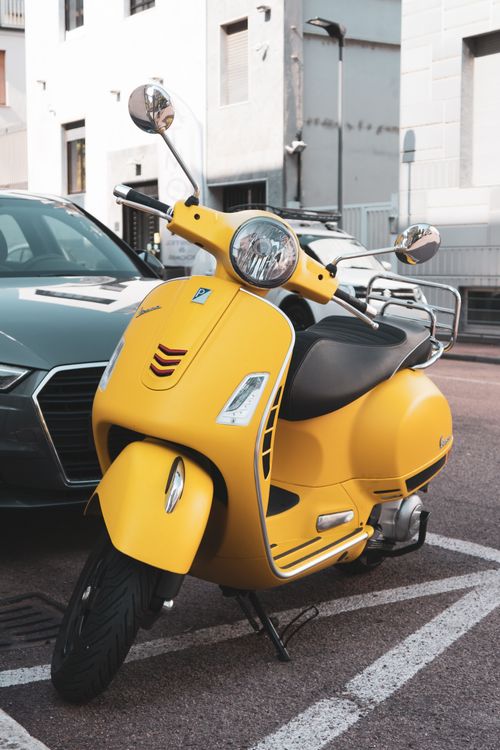 Free Bright yellow Vespa scooter parked on a street in Milan, Italy, with urban background. Stock Photo