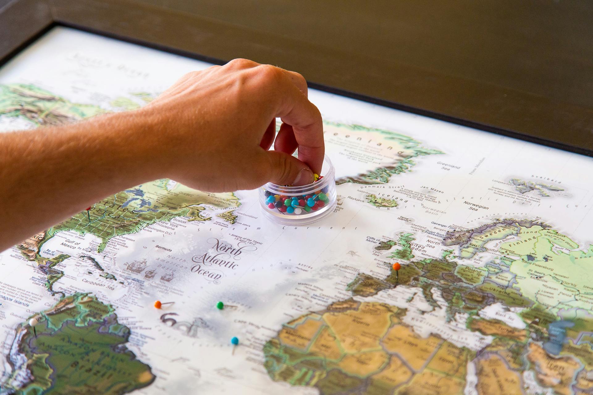 A hand placing colorful pins on a world map, symbolizing travel planning and global exploration.