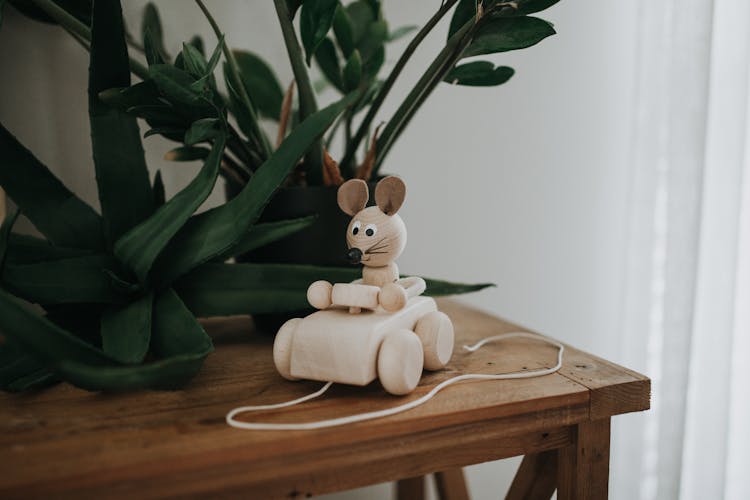 A Wooden Mouse Toy Riding A Car On A Wooden Table