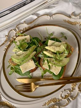 Avocado and brie cheese on toast with fresh greens, elegantly styled.