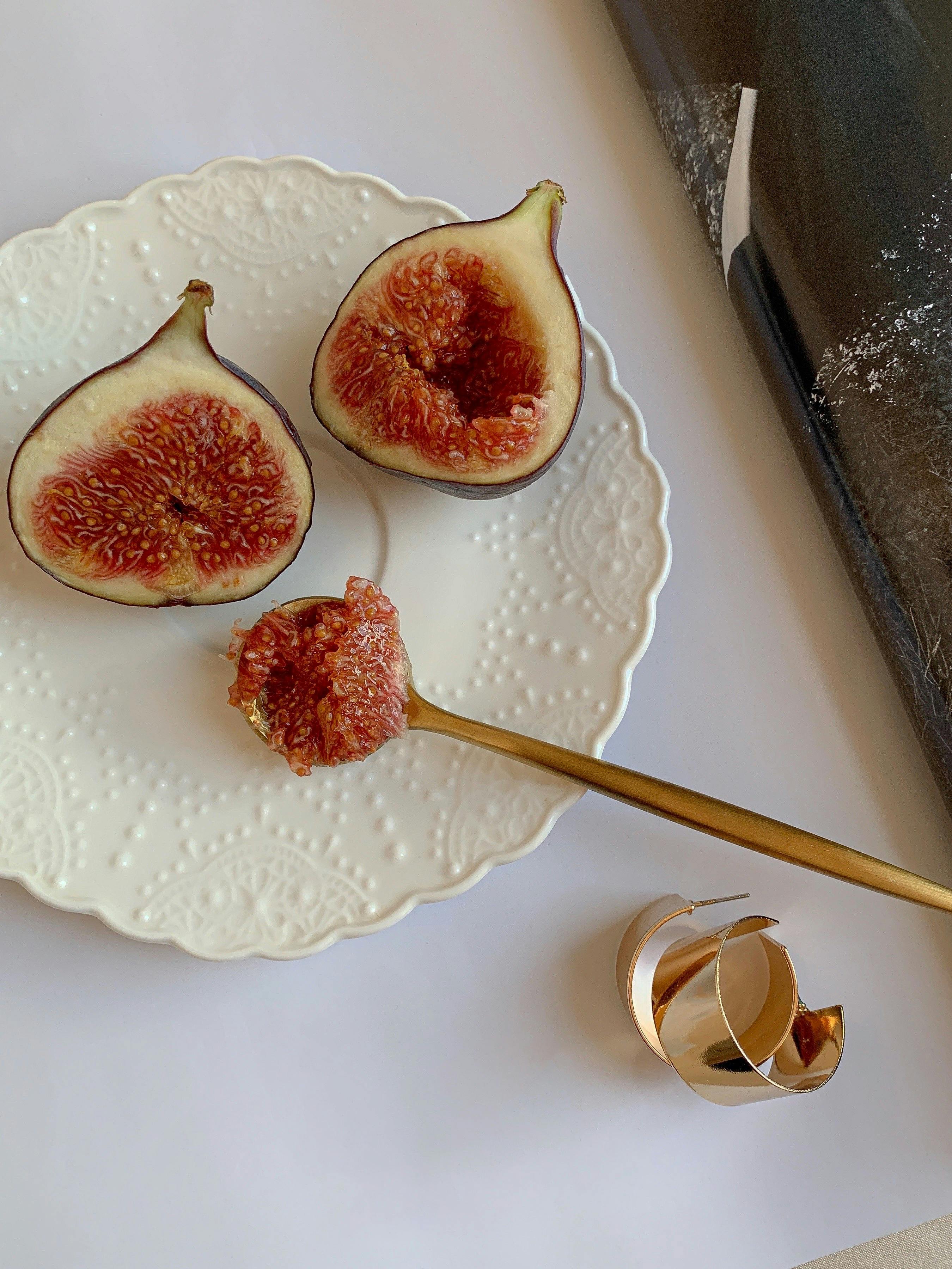 Minimalist still life showcasing a sliced fig on a ceramic plate with gold utensils, captured in top view.