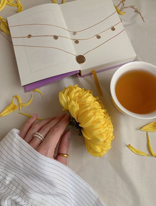 Free A serene composition featuring an open book, cup of tea, yellow flower, and hand with jewelry. Stock Photo