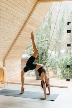 A woman performs a yoga pose indoors, surrounded by natural light and wood accents.