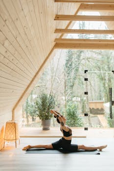 Woman doing yoga splits on a mat in a serene wooden cabin with a forest view.