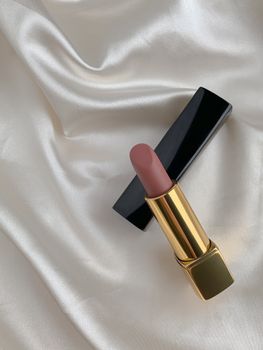 Nude lipstick elegantly displayed on smooth silk fabric, showcasing minimalist beauty.