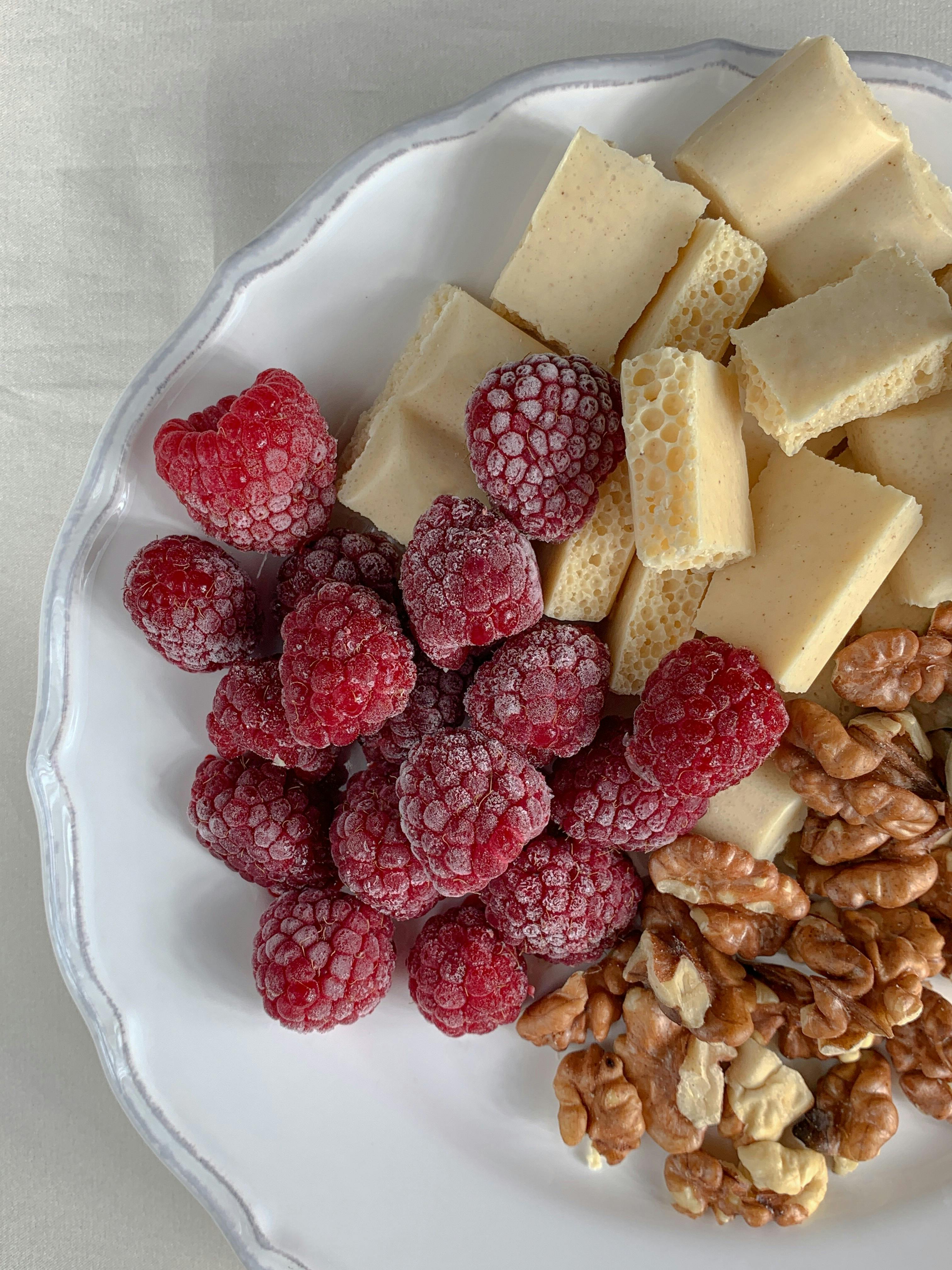 close up shot of raspberries nuts and white chocolate on a white plate