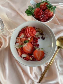 Healthy breakfast bowl with strawberries, yogurt, pomegranate seeds, and almonds on a satin fabric.