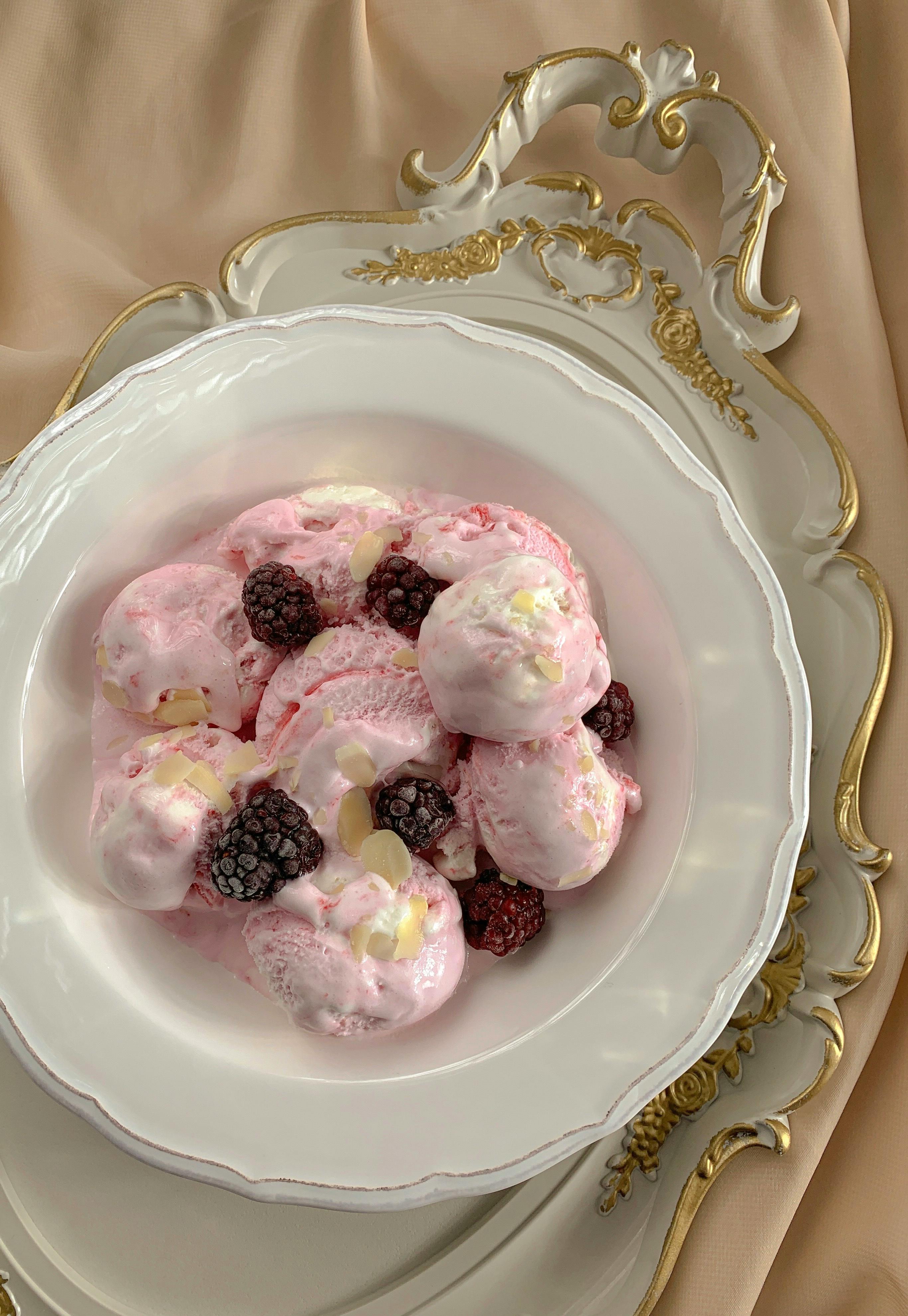 Pastel pink ice cream with blackberries beautifully presented on a vintage china plate for an indulgent treat.