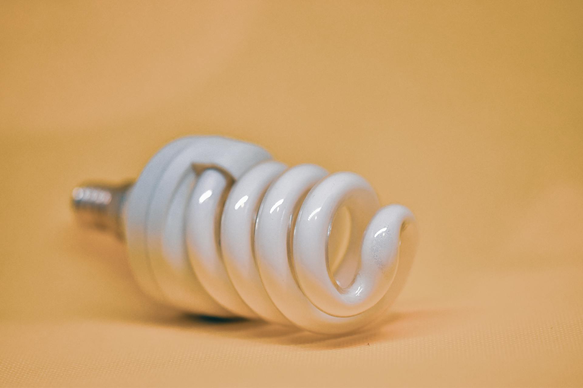 Close-up of a spiral compact fluorescent lamp with orange background, ideal for energy and lighting concepts.