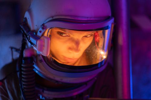 Free A spacewoman gazes intensely, illuminated by vivid colors through her helmet's visor. Stock Photo