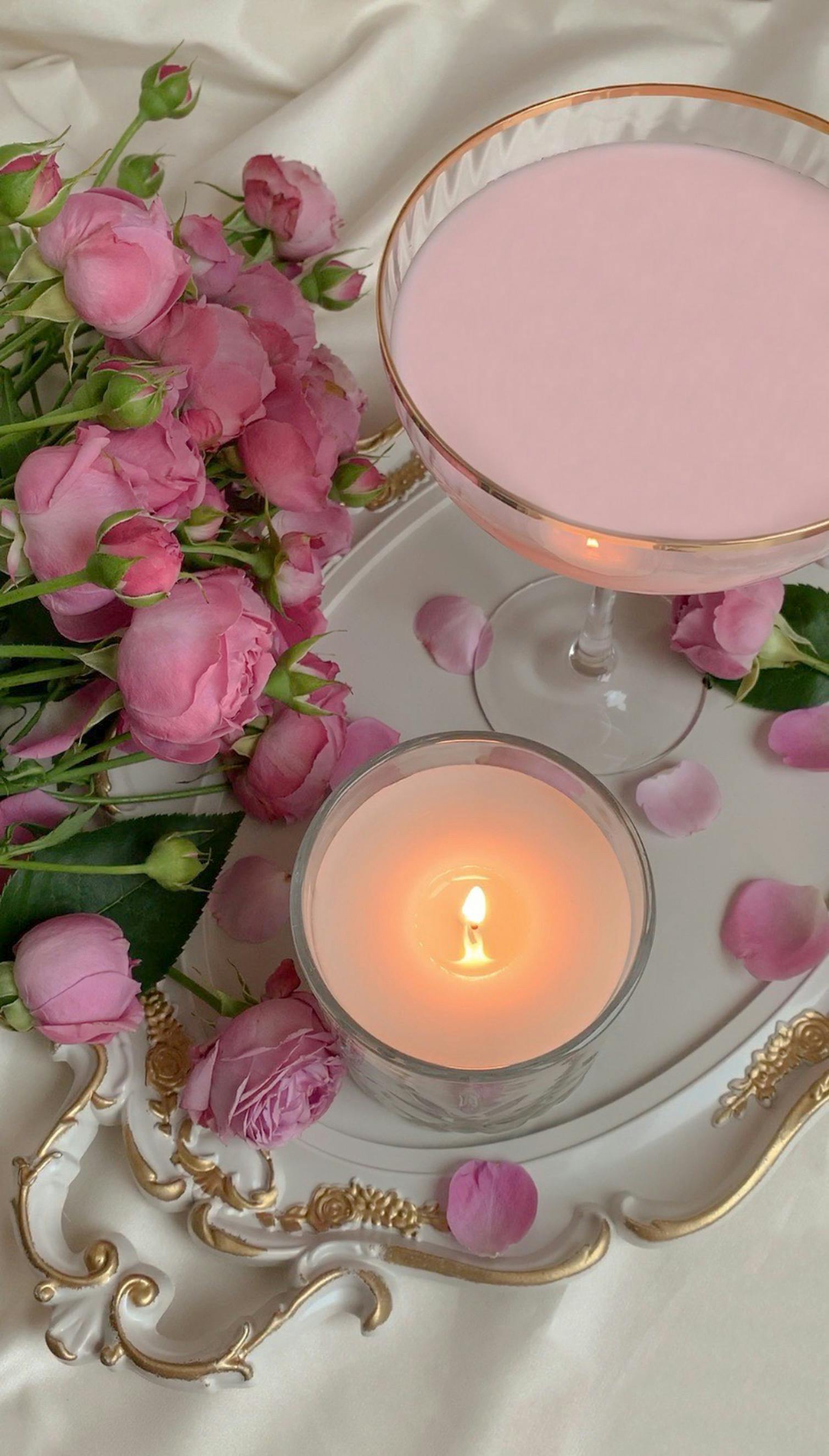 A sophisticated arrangement featuring pink roses, a lit candle, and a pink drink on a decorative tray.