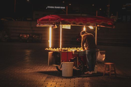 A street vendor selling food at night with a glowing cart in urban surroundings.