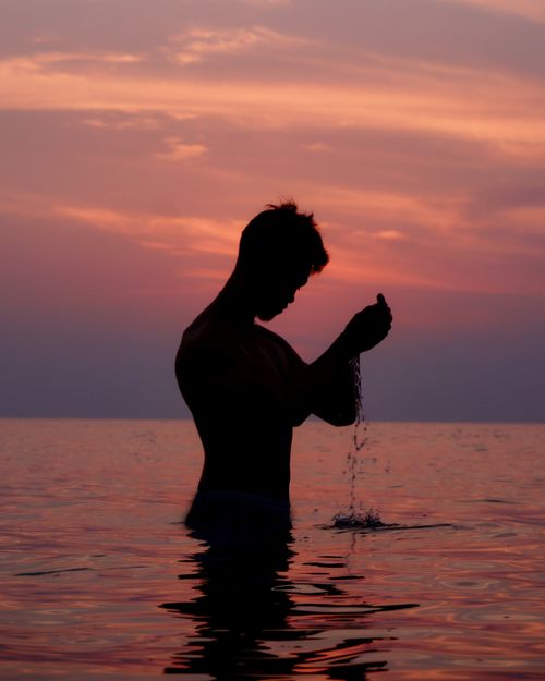 Free Dramatic silhouette of a man in ocean water at sunset with a colorful sky. Stock Photo
