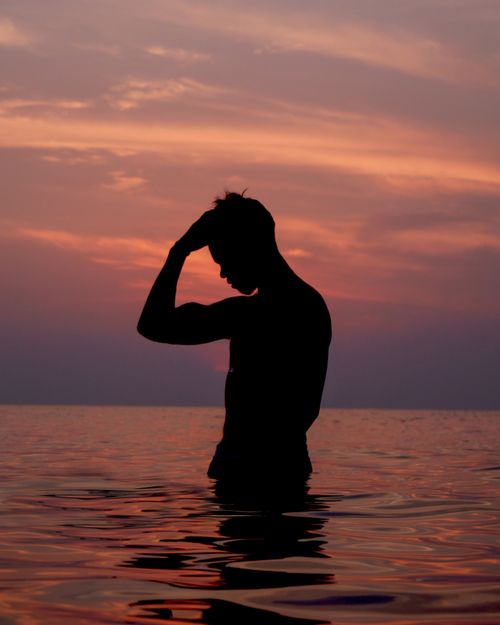 Free Silhouette of a man in the ocean at sunset, capturing tranquility and beauty. Stock Photo