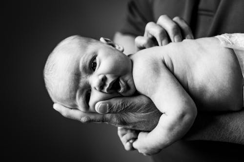 Grayscale Photo of Baby Lying on Person's Hand