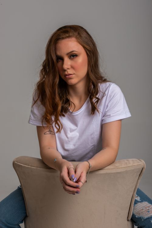 Free Portrait of a young woman in casual attire sitting on a chair in a studio setting. Stock Photo