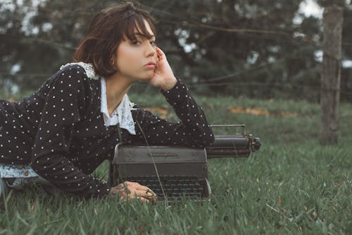 Woman in Black and White Polka Dot Long Sleeve Shirt Lying on Green Grass Field