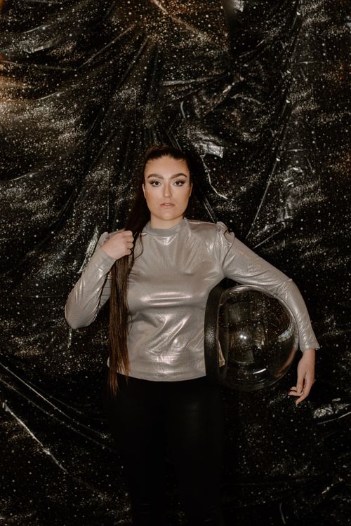 Free Woman in shiny silver attire holding a space helmet, evoking a futuristic theme. Stock Photo