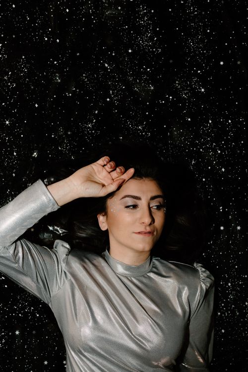 Free A woman in a shiny silver outfit lying against a starry backdrop, evoking a futuristic or space theme. Stock Photo