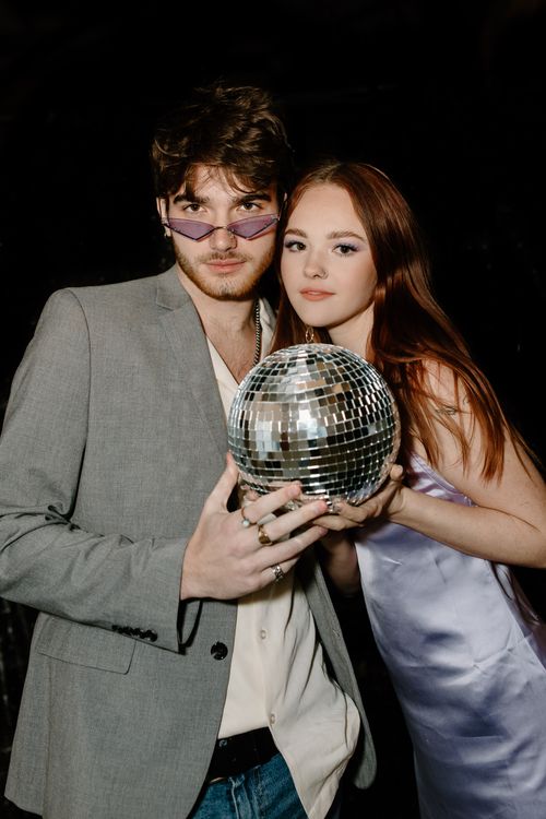 Free Fashionable young couple posing with a disco ball, exuding a chic party vibe. Stock Photo