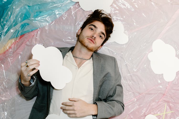 Man Lying Down In Gray Suit Jacket Holding White Cloud Shape Paper