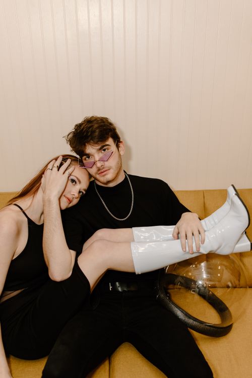 Free Stylish couple wearing modern outfits with a futuristic vibe sitting together indoors. Stock Photo