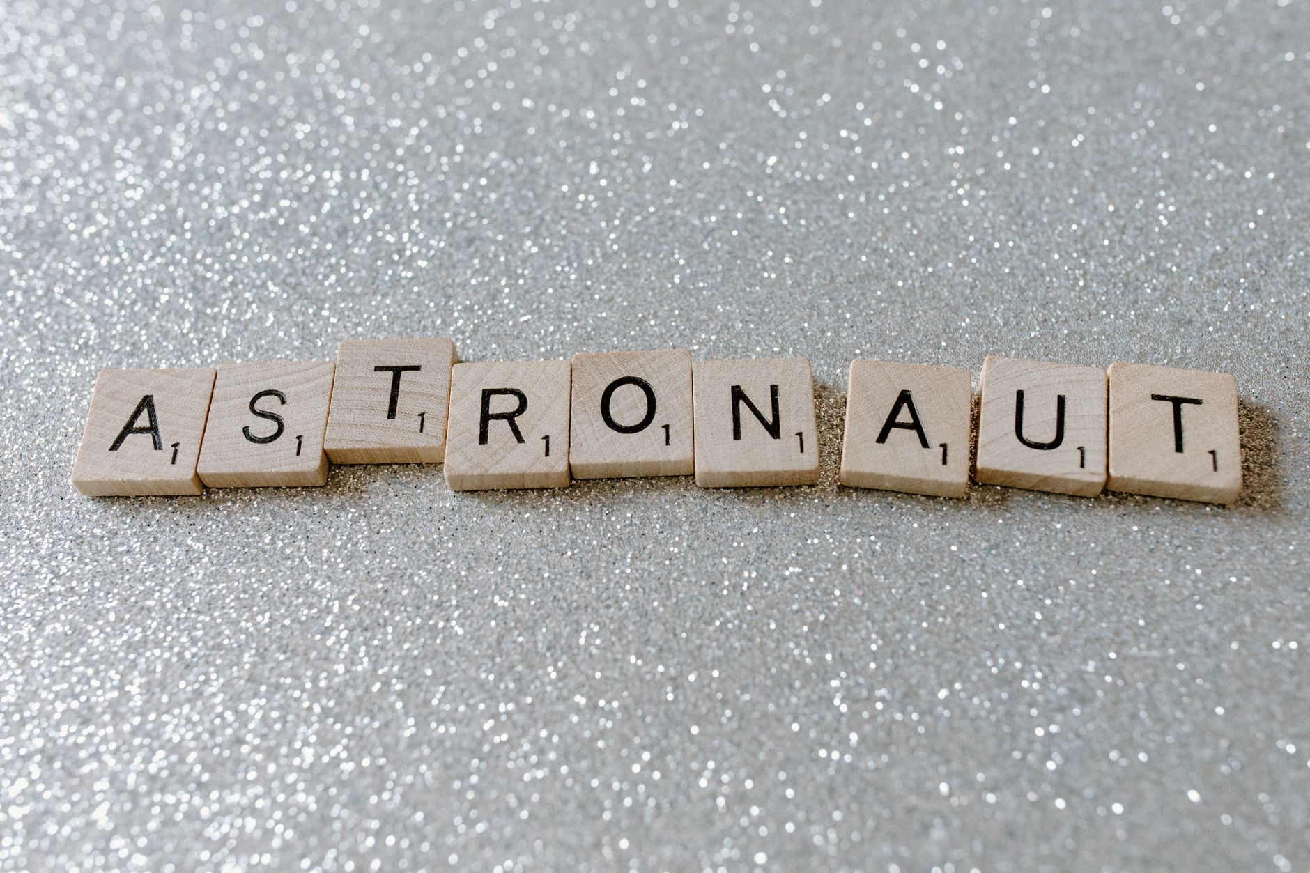 Wooden tiles spelling 'astronaut' on a glittery surface, perfect for space-themed designs.