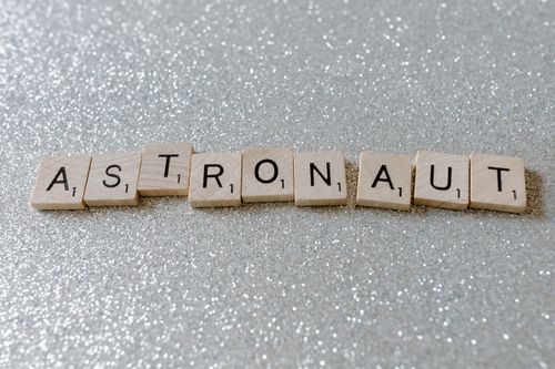 Free Wooden tiles spelling 'astronaut' on a glittery surface, perfect for space-themed designs. Stock Photo