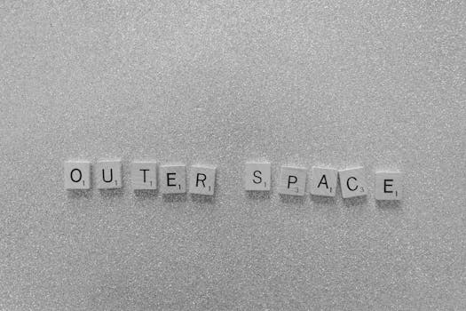 Scrabble tiles spelling 'Outer Space' on a shimmering glitter surface in black and white.