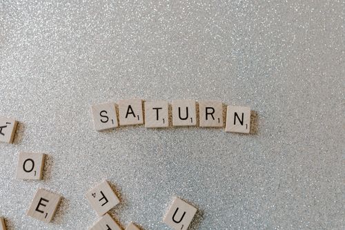 Free Scrabble tiles forming the word SATURN on a sparkling glitter background, space theme. Stock Photo