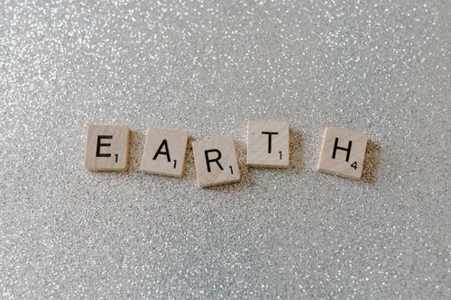 Free Wooden Scrabble tiles spelling 'EARTH' on a sparkling glitter background. Stock Photo
