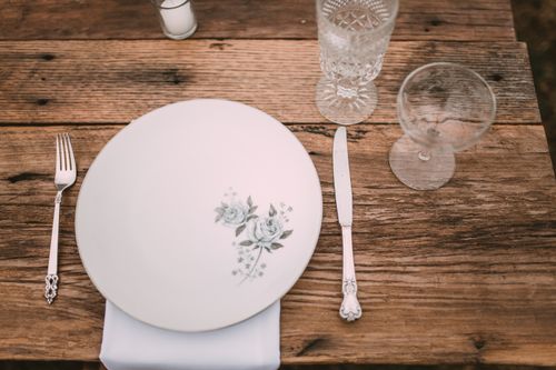 Free A rustic table setting features vintage cutlery, glasses, and a floral plate on a wooden surface. Stock Photo