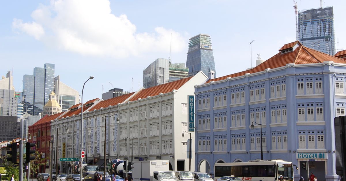 Vibrant city scene in Singapore featuring historic buildings, moving vehicles, and clear blue sky.