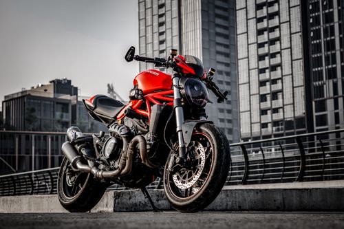 Free A red motorcycle is parked against a backdrop of modern urban architecture. Stock Photo