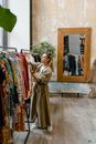 Woman in Brown Trench Coat Standing in Front of Clothing Rack