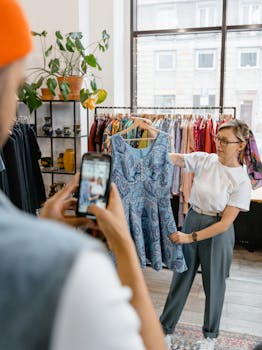 A stylish woman holds a dress while a photographer captures the moment in a trendy boutique.