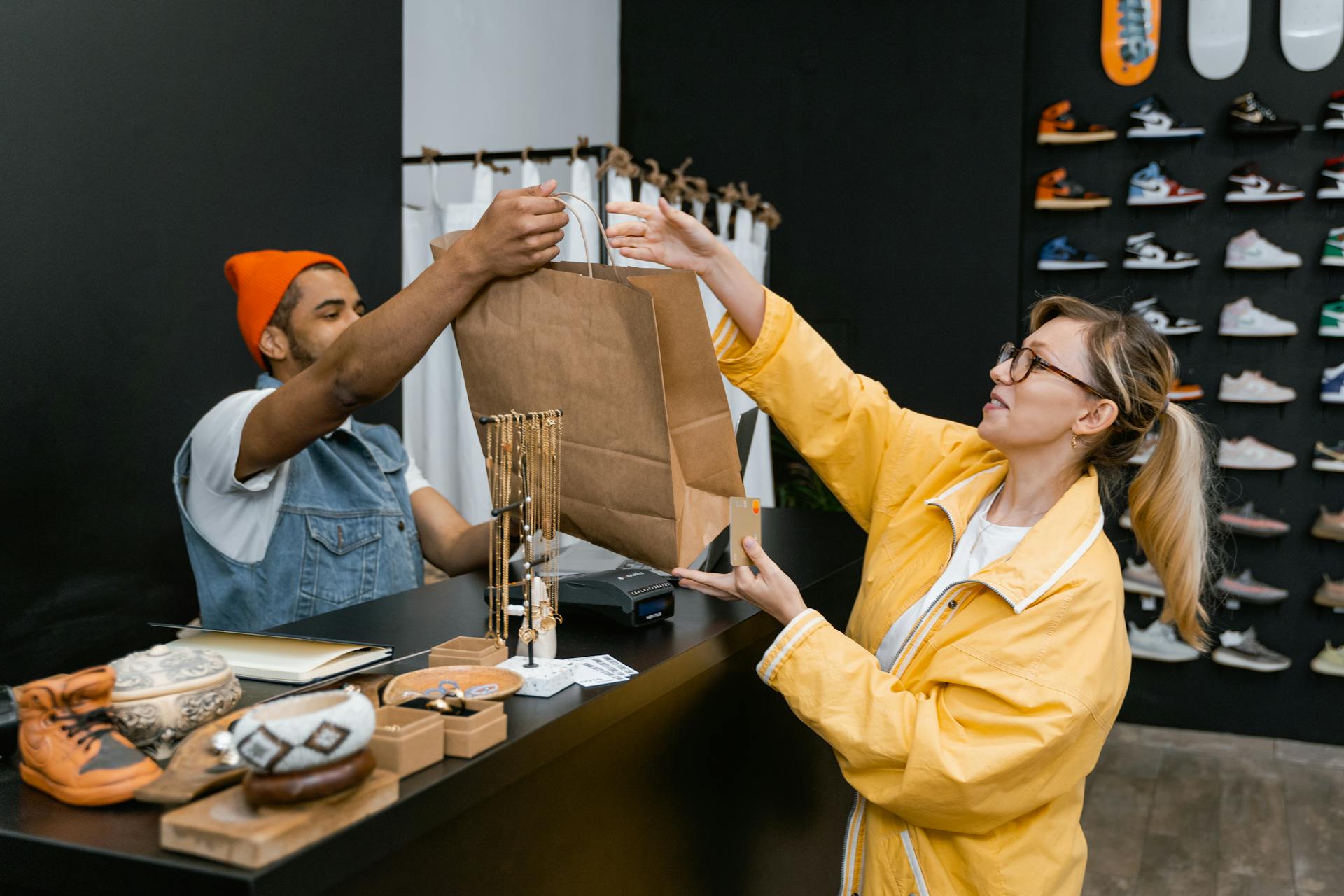 A customer and cashier exchange items at a fashionable sneaker store counter.