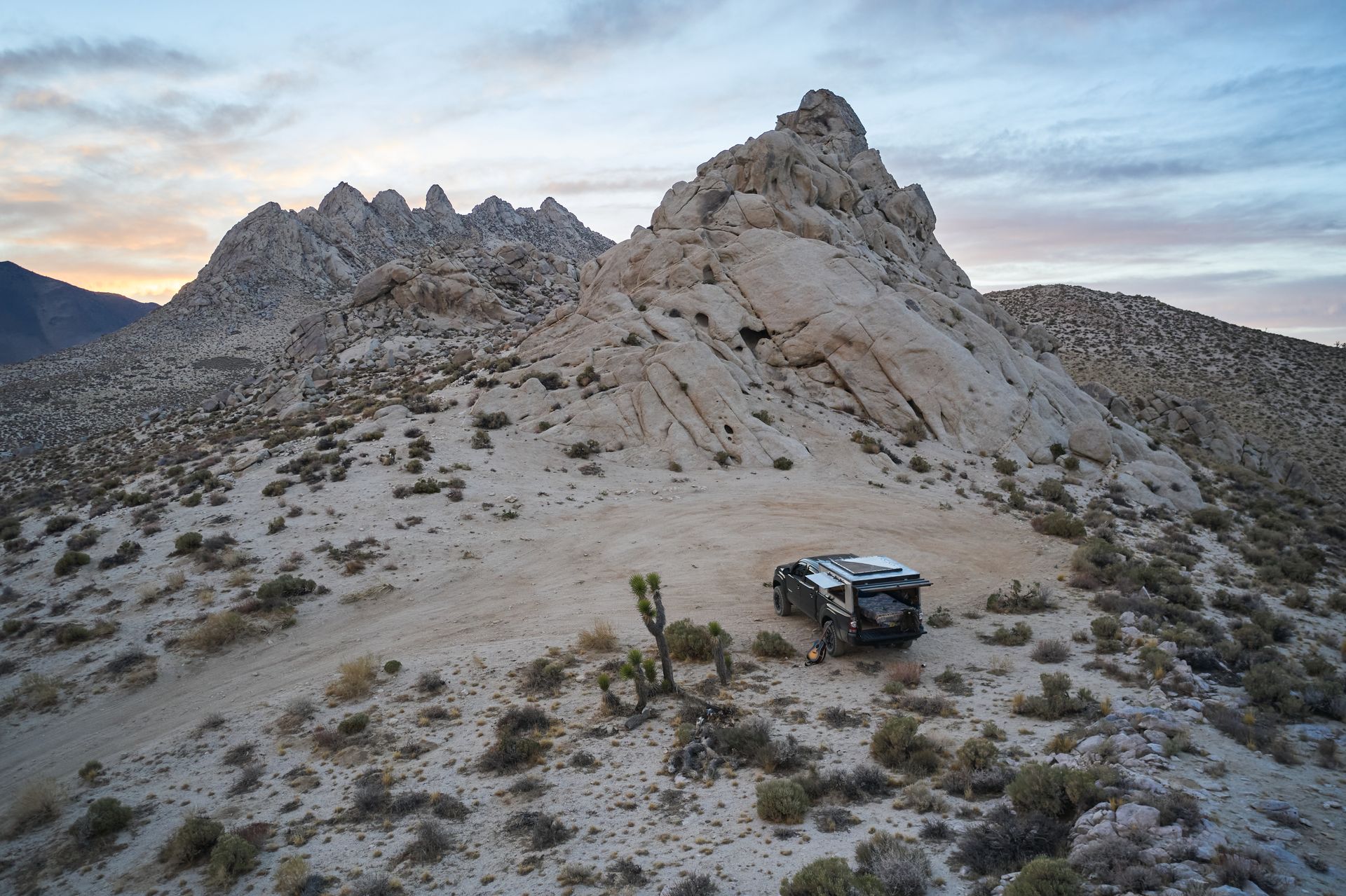 A rugged desert landscape featuring a camper truck near rock formations at dusk in Inyokern, CA.