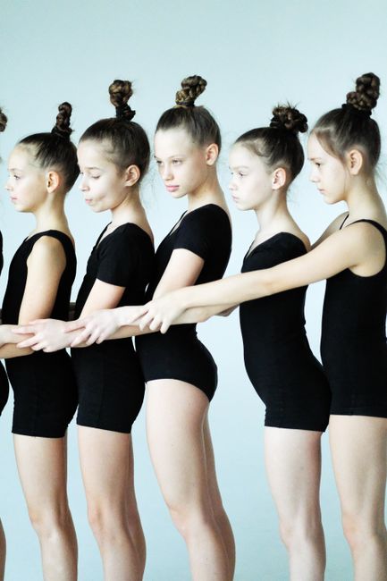 Group of young ballet dancers in black leotards practicing in a studio.