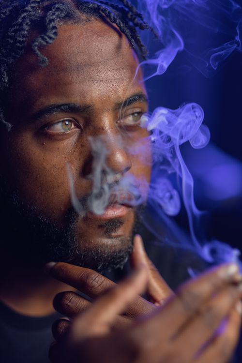Free Close-up of a man with dreadlocks smoking, blue smoke swirling around his face. Stock Photo