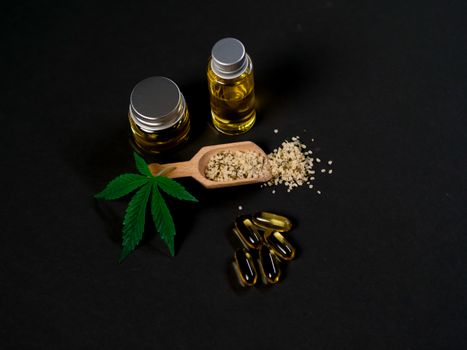High-quality cannabis oil and capsules with hemp seeds and leaf on a dark backdrop.