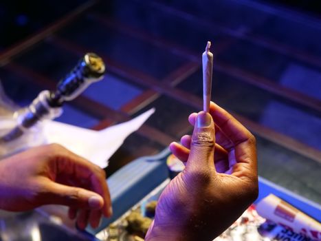 A detailed view of hands preparing and holding a cannabis joint indoors, highlighting cannabis culture.