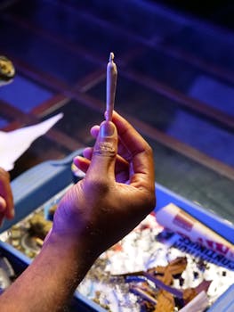 Close-up of a hand holding a joint with cannabis in an indoor setting.