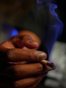 Detailed close-up photo of a hand with a lit joint emitting smoke.