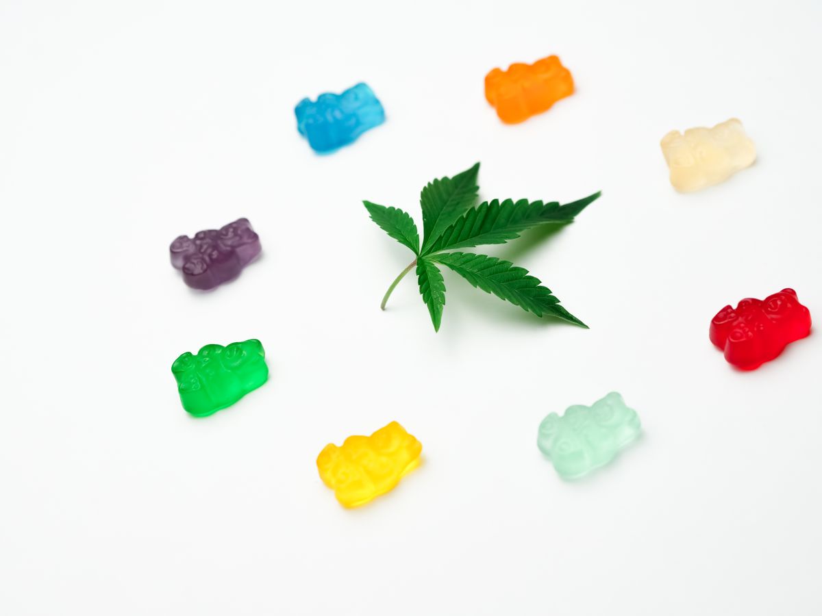 Vibrant assortment of gummy candies surrounding a cannabis leaf, creatively displayed against a white background.