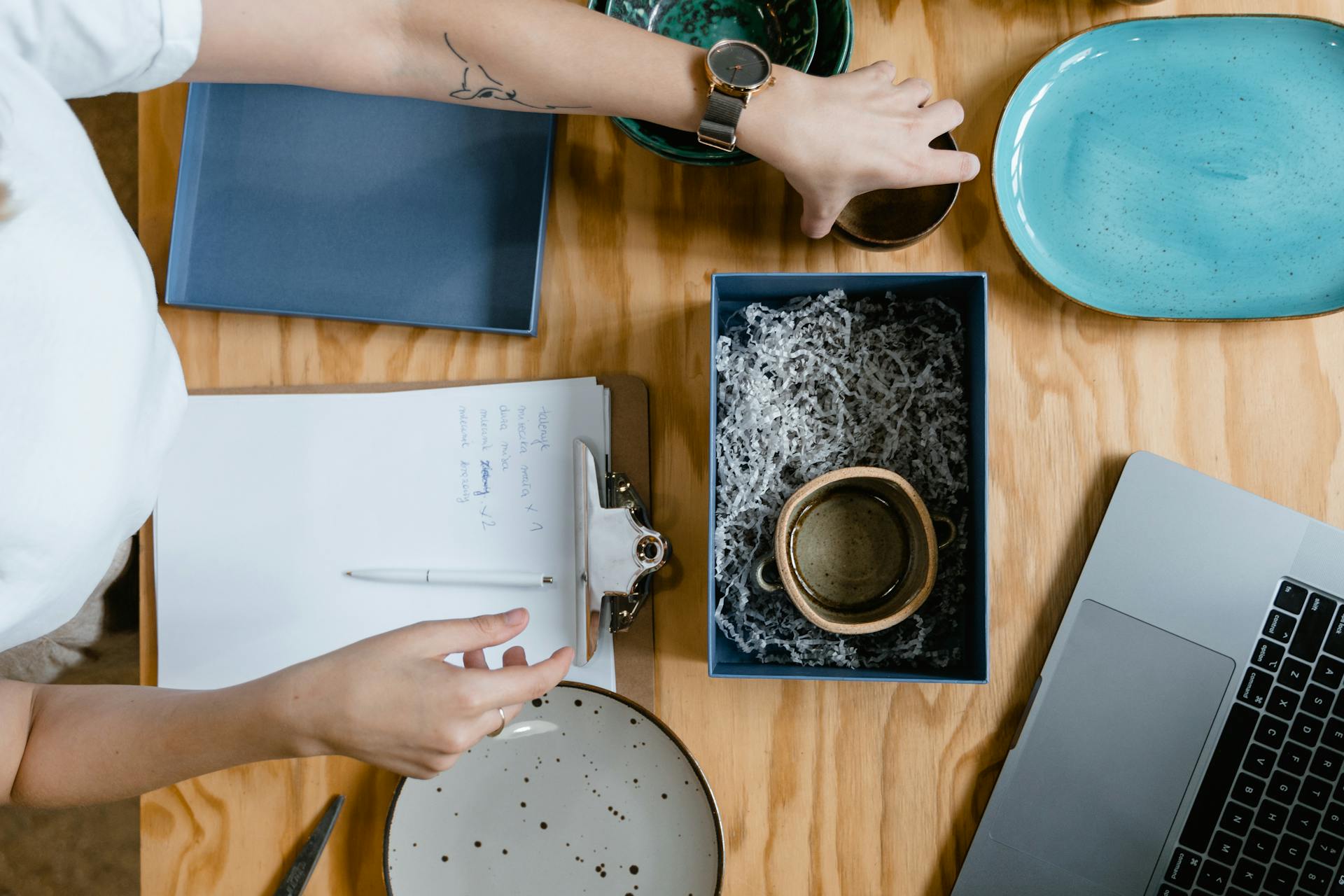 Overhead view of a woman packing a ceramic mug into a box for shipping. Ideal for e-commerce concepts.