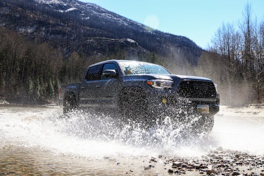 A Toyota Tacoma drives through a water puddle with splashing effects in a rugged outdoor setting.