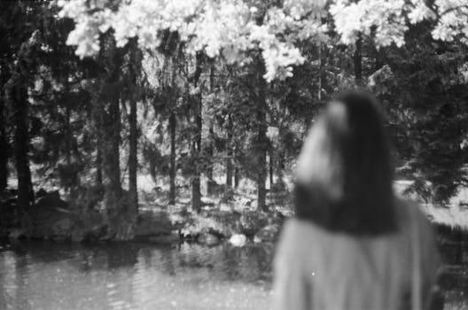 Black and white photo of a woman standing by water in a park.